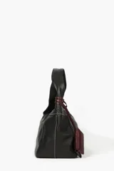 Cartera de cuero vacuno color negro, con costuras a contratono en color blanco y un práctico bolsillo frontal desmontable en color bordó con tiras envolventes. Cuenta con asa para el hombro.