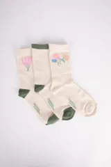Pack de tres pares de medias de algodón color crema, con puño y puntera en verde. Un par tiene bordado de flores rosas, otro de flores de varios colores y el tercero es liso.