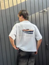 Remera celeste de corte recto con estampado de un yate y texto en color gris.