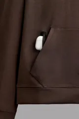 Sudadera de hombre Zara Athleticz de ajuste relajado (relaxed fit), color marrón, confeccionada en tejido técnico compacto con mezcla de algodón y elasticidad. Cuenta con cuello con capucha ajustable con cordones negros, manga larga, bolsillo frontal tipo canguro con un pequeño bolsillo termofijado con cierre, y acabados con rib en puños y cintura.