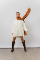 Buzo tipo sweater de punto color blanco, con diseño de trenzas verticales, cuello redondo, mangas largas y tajos laterales. Presenta un corte oversize y largo extendido.