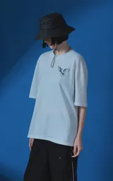 Remera blanca de corte oversize con cuello redondo y manga corta. Presenta una estampa gráfica en la espalda con diseño de palomas, flores y texto en español.