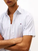 Camisa de hombre Tommy Hilfiger de manga corta, confeccionada en popelina de algodón con tecnología Flex, a rayas verticales blancas y celestes. Tiene cuello abotonado, corte regular y logo bordado en el pecho.