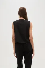 Chaleco negro sin mangas, de corte corto y abierto, con bordado floral en hilo blanco que recorre el borde del cuello y los frentes.