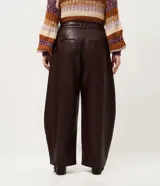 Pantalón de cuero sintético con corte barrel, de tiro alto y pierna ancha con estructura curva. Presenta bolsillos laterales tipo cuchillo y costuras decorativas con pespuntes visibles.