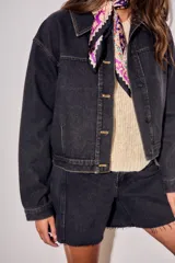Campera oversize de denim negro, con cuello camisero, cierre frontal con botones y bolsillos ojal.