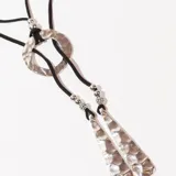 Collar con cordón negro, dije circular plateado y colgantes con forma de lágrima texturizadas.