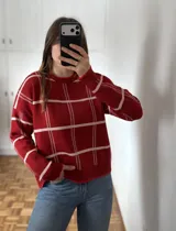 Sweater de punto color rojo con diseño de cuadrícula en color blanco, de corte holgado, cuello redondo y mangas largas con puños acanalados.