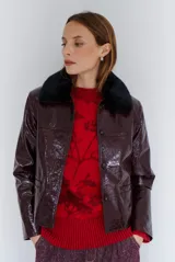 Chaqueta de efecto cuero brillante con acabado charol, cuello con solapas de piel sintética, cierre frontal con botones y bolsillos laterales.