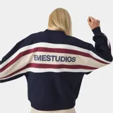 Buzo de tejido de punto con cierre frontal, diseño de franjas horizontales en azul marino, blanco y bordó, con el nombre de la marca estampado en la espalda.