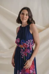 Vestido largo de gasa estampada con flores en tonos lila y rojo sobre fondo azul. Tiene cintura elastizada y cuello halter.