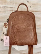 Mochila de cuero color marrón con textura tipo croco en el panel frontal. Cuenta con cierre superior, asa de mano superior, correas ajustables y una correa lateral extraíble con diseño estampado. Incluye logo de la marca grabado en el frente.