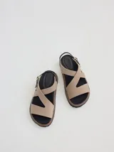 Sandalia de diseño ergonómico con tiras cruzadas en color beige, plantilla negra y suela dentada con pespunte en contraste. Cuenta con una tira trasera ajustable con hebilla metálica.