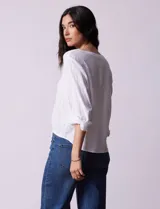 Blusa blanca de algodón marca Dash, con escote en V, abertura con botones, mangas 3/4 regulables con presilla y botón, y terminación de ruedo anudado.