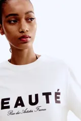Remera de algodón color blanco crudo, con cuello redondo y manga corta. Presenta un estampado frontal con la palabra "BEAUTÉ" en mayúsculas y debajo en cursiva "Rue des Artistes France".