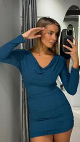 Vestido corto de manga larga en color azul petróleo con acabado brillante tipo lurex. Presenta un escote drapeado y diseño ajustado con frunces laterales en la falda.