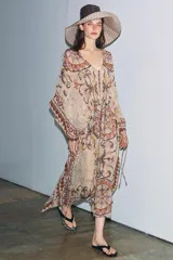 Vestido tipo túnica de viscosa con escote en pico y mangas tipo capa. Presenta un diseño estampado con motivos ornamentales en tonos tierra, beige y rosado, con pliegues en la cintura y bajo asimétrico.