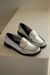 Mocasín de cuero con textura efecto cocodrilo en color plateado, con herraje metálico dorado con logo VDM y suela plana oscura.