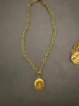 Collar de cadena de eslabones gruesos con dije de medalla ovalada con relieve de la Virgen, acabado en tono dorado con textura artesanal.