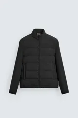 Cazadora acolchada de cuello subido, color negro, con mangas largas de tejido elástico. Incluye bolsillos en la cadera, un bolsillo interior y bajo con elástico. Cierre frontal de cremallera.