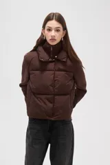 Campera combinada con cuerpo acolchado tipo puffer y mangas de tejido de punto acanalado, en color marrón. Presenta cuello alto con cierre frontal y botones a presión.