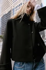 Abrigo corto de paño en color negro, con cuello subido, cierre frontal cruzado con botones, mangas largas con trabillas en los puños y bolsillos delanteros de vivo.
