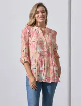 Blusa de gasa estampada con flores en tonos rosa, amarillo y azul. Tiene cuello a la base, escote en V y botones. La delantera tiene detalle plisado y las mangas son 3/4 regulables con presilla y botón.