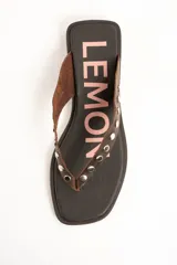 Sandalias planas de cuero marrón tipo ojota con tiras anchas adornadas con tachas metálicas plateadas y plantilla con diseño estampado.