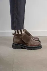 Botinetas de caña baja con suela track gruesa, combinando cuero negro en la puntera, gamuza marrón en el lateral y detalles de textura animal print tipo serpiente en tonos marrones. Presenta un cierre de solapa con velcro en el empeine.