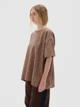 T-shirt oversize de denim con estampado de rombos en tonos azules, cuello redondo y mangas cortas. Presenta un bordado de estrellas blancas en el pecho y costuras visibles en color marrón claro.