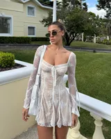 Minivestido color nude con encaje floral blanco, escote corazón con lazo ajustable, mangas largas acampanadas de encaje y corte ajustado al cuerpo.