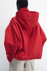 Cazadora roja de cuello subido con capucha y manga larga, bolsillos delanteros y cierre frontal cruzado con botones a presión dorados.