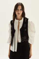 Chaleco de cuero negro con flecos largos en los laterales y detalles bordados en hilo blanco en la espalda.