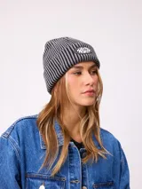 Gorro tipo beanie de tejido acanalado con diseño a rayas verticales en tonos azul y gris. Presenta un parche frontal con el logo de la marca Rusty.