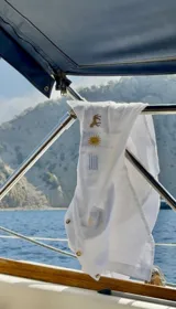 Camisa blanca de lino con botones dorados, manga larga y cuello. Presenta un bordado vertical en el pecho con un caballito, el Sol de Mayo y franjas verticales celestes, alusivos a la bandera uruguaya.