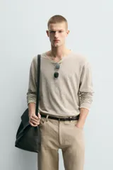 Jersey de punto de corte relajado, con cuello redondo amplio y mangas largas. Presenta un diseño de rayas horizontales finas en contraste sobre fondo beige.