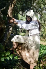 Capucha tejida a mano en lana merino con diseño de rayas horizontales en color mostaza y beige. Presenta una forma envolvente con lazos largos para anudar bajo el cuello, funcionando como un accesorio independiente de abrigo.