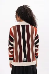 Buzo de tejido de punto con diseño de rayas verticales onduladas en tonos tierra, negro y crema. Presenta cuello redondo, mangas largas y corte holgado.