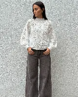 Camisa blanca de algodón con detalles de encaje y bordado calado en el frente y las mangas. Presenta cuello alto con volado, mangas largas abullonadas con puños y cierre de botones en la espalda.
