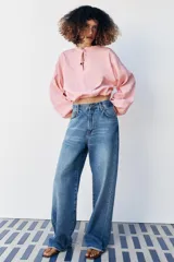 Blusa de manga larga con estampado de cuadros vichy en tonos rosado y blanco. Presenta cuello redondo con volante, cordón ajustable en el escote con apliques decorativos, y puños fruncidos con tiras para atar.