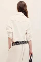 Campera corta de gabardina blanca estilo trucker, con bolsillos frontales con solapa, mangas largas y cierre de botones metálicos.