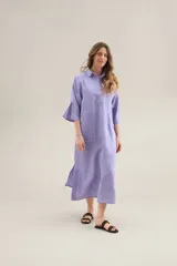 Vestido largo lila de lino, con cuello camisero, mangas cortas, bolsillos frontales con costuras a contratono y aberturas laterales.