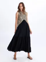 Vestido largo sin mangas, de color negro con la parte superior bordada en tonos dorados y negros con patrones geométricos. Presenta escote en V y falda con volados escalonados.