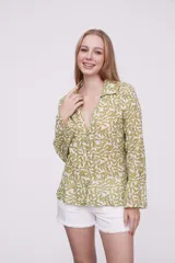 Blusa de algodón con estampado de hojas en tonos verdes sobre fondo blanco, cuello camisero, cierre frontal con botones y mangas largas.