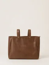 Bolso tipo tote de cuero color marrón, con diseño minimalista, doble asa de mano y cierre superior. Presenta el logo de la marca grabado en un parche central y detalles de remaches metálicos.