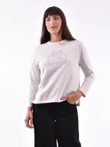 Remera de manga larga color crema con cuello redondo y un estampado central de un ramo de flores rosadas y naranjas en un jarrón azul oscuro.