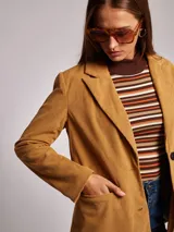 Blazer color ocre de pana con cuello y solapa, manga larga, bolsillos delanteros con solapa y cierre frontal con dos botones.