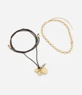 Collar de diseño multicapa que combina una cadena corta de eslabones redondos dorados con tiras de cordón marrón oscuro ajustables con terminales metálicas y dijes colgantes que incluyen una medalla texturizada, un corazón y una pieza en forma de colmillo.