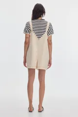 Monoprenda corta de denim color beige, de fit oversize, con tirantes regulables y bolsillo canguro en el frente.
