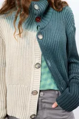Saco de hilo con cuello alto y cierre de botones, de tejido de punto y diseño oversize. Presenta un teñido artesanal degradado que combina gris y beige, con mangas largas y puños amplios, además de un detalle de aplicación floral oscura en el pecho.